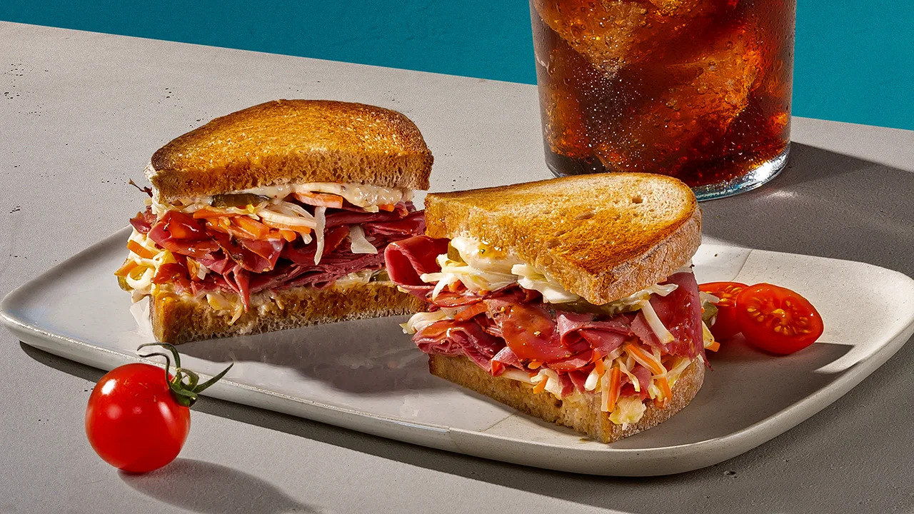 Ein Whisky-Cocktail neben einem Teller mit Pastrami-Sandwich mit Balsamico.