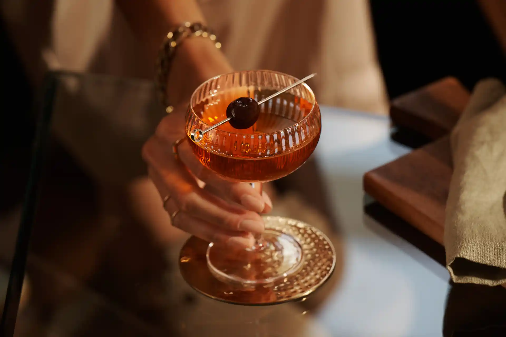 Een vrouw houdt de steel van een coupeglas met een Manhattan-cocktail vast