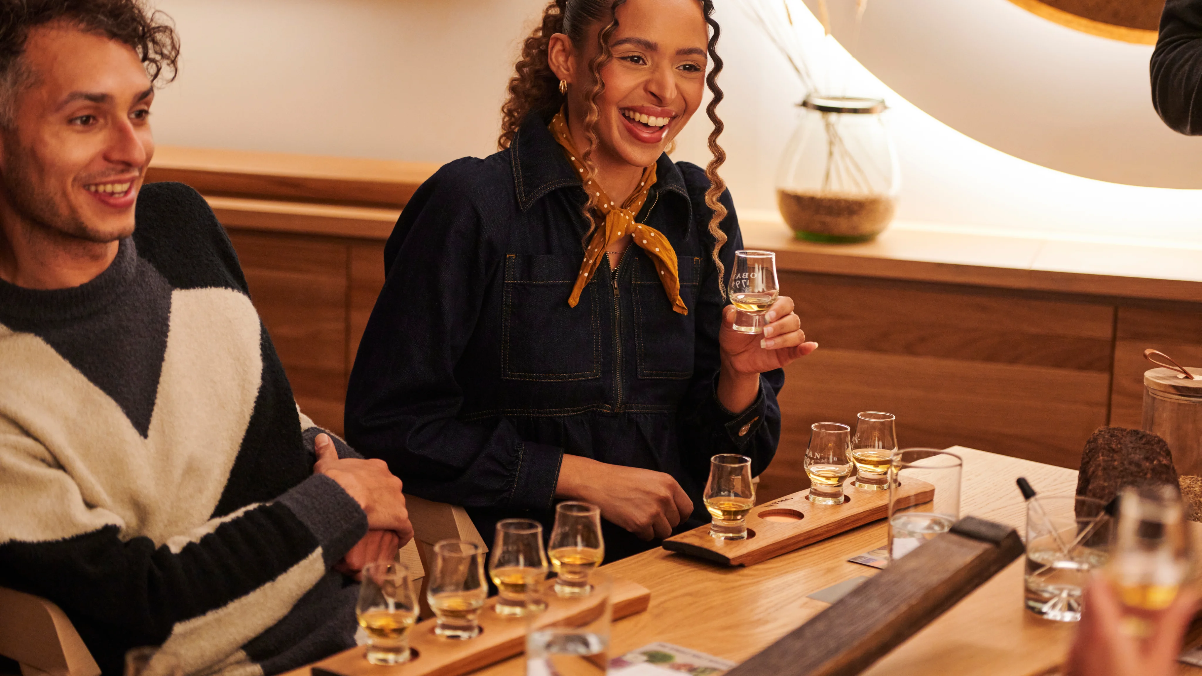 Two people enjoying a whisky tasting flight with glasses on a wooden table.