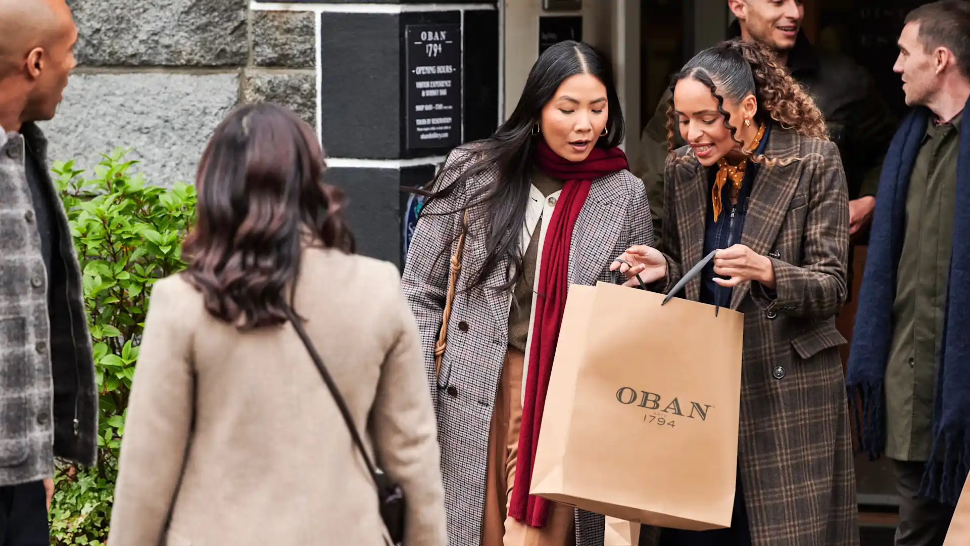 Eine Gruppe von Freunden verlässt die Oban-Destillerie. Zwei Frauen schauen lächelnd in eine Oban-Geschenktüte und betrachten ihre Einkäufe.