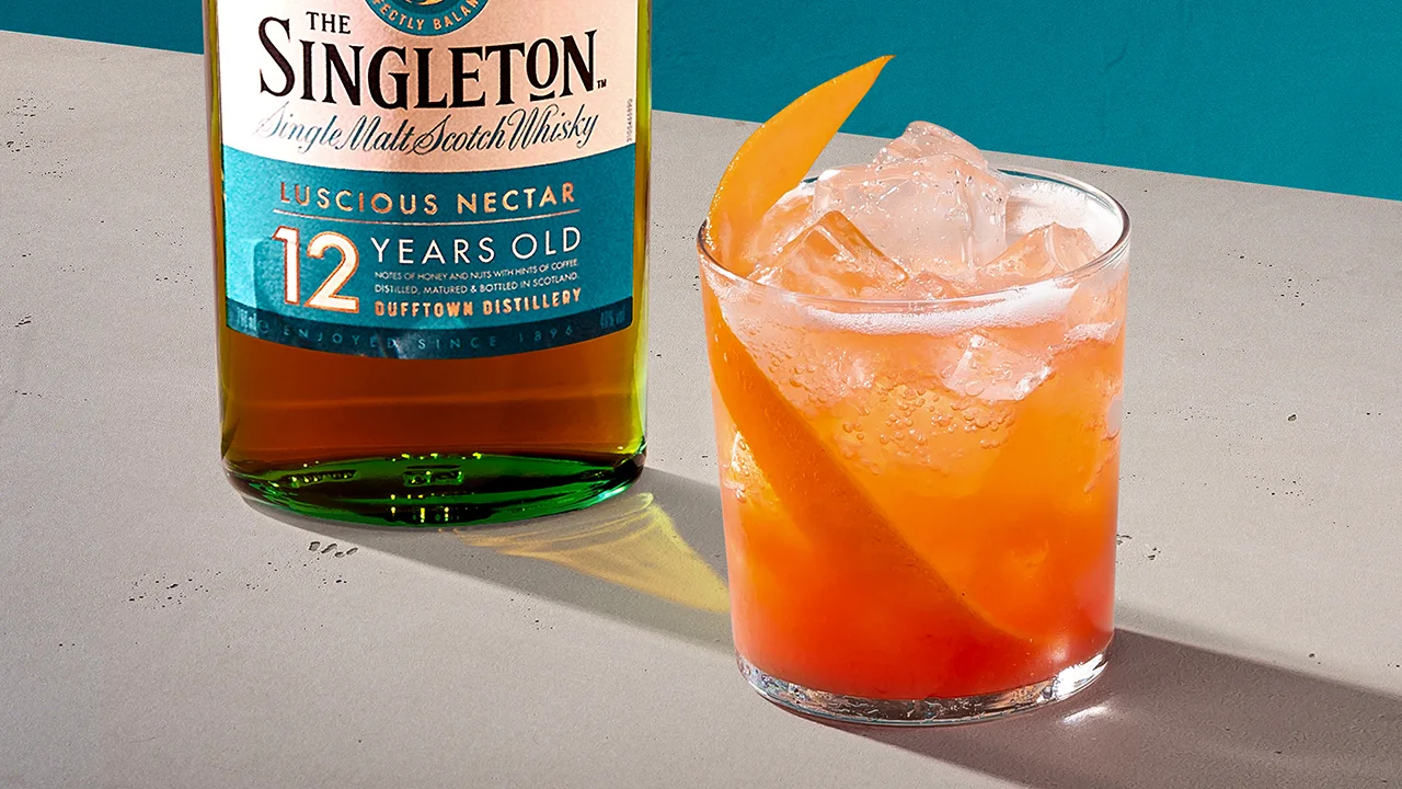 Ein orangefarbener Whisky-Cocktail neben einer Flasche The Singleton 12 Year Old Single Malt Scotch Whisky.
