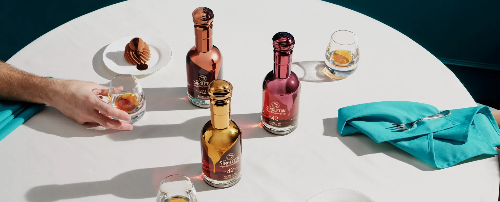 The three Gourmand Collection singleton whiskies on a table with hands holding plates of cake 