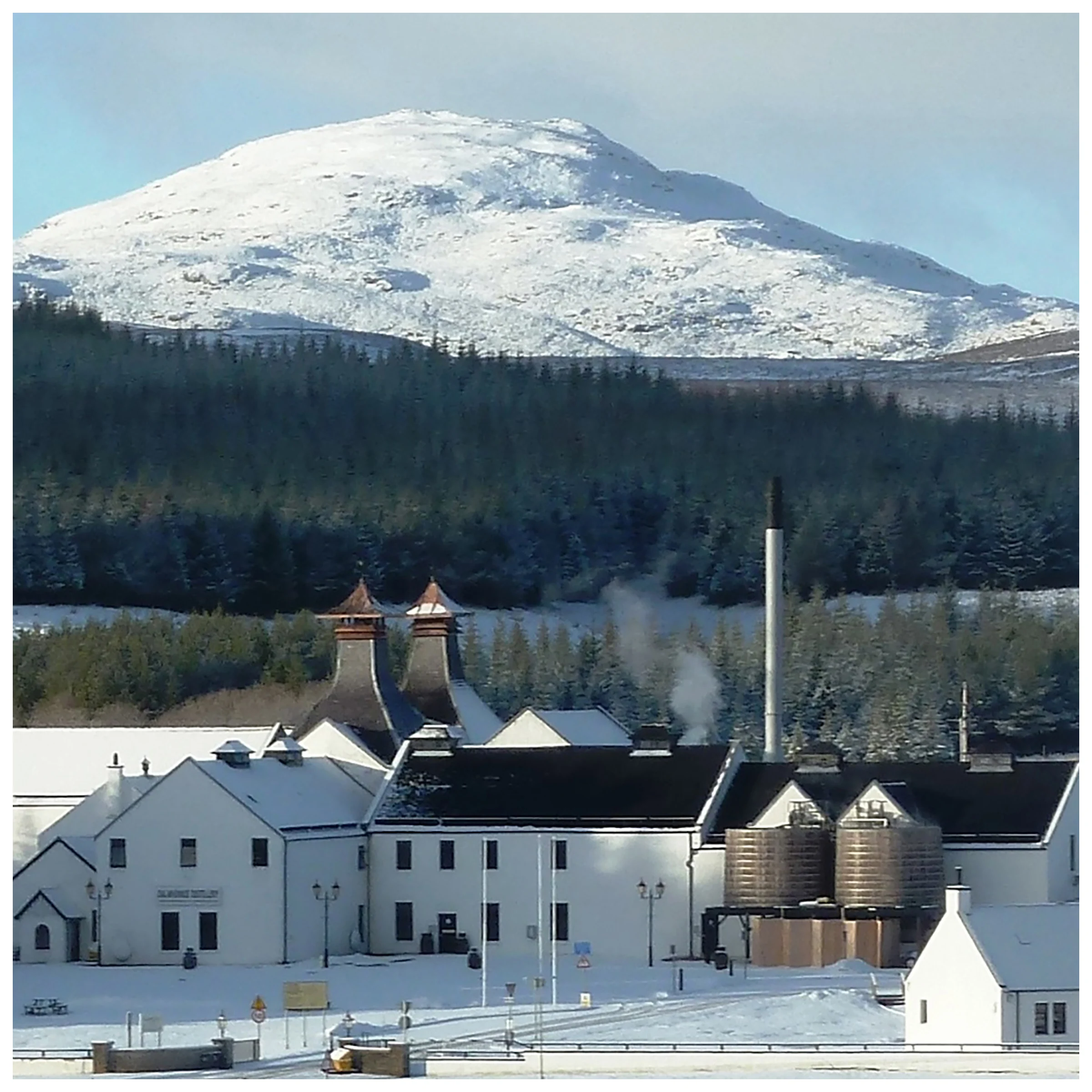 Dalwhinnie distillery sits in front of a large snow covered mountain