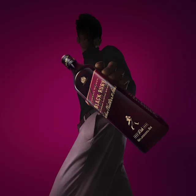 A person holds a bottle of Johnnie Walker Black Ruby Blended Scotch in their hand and shows it off.