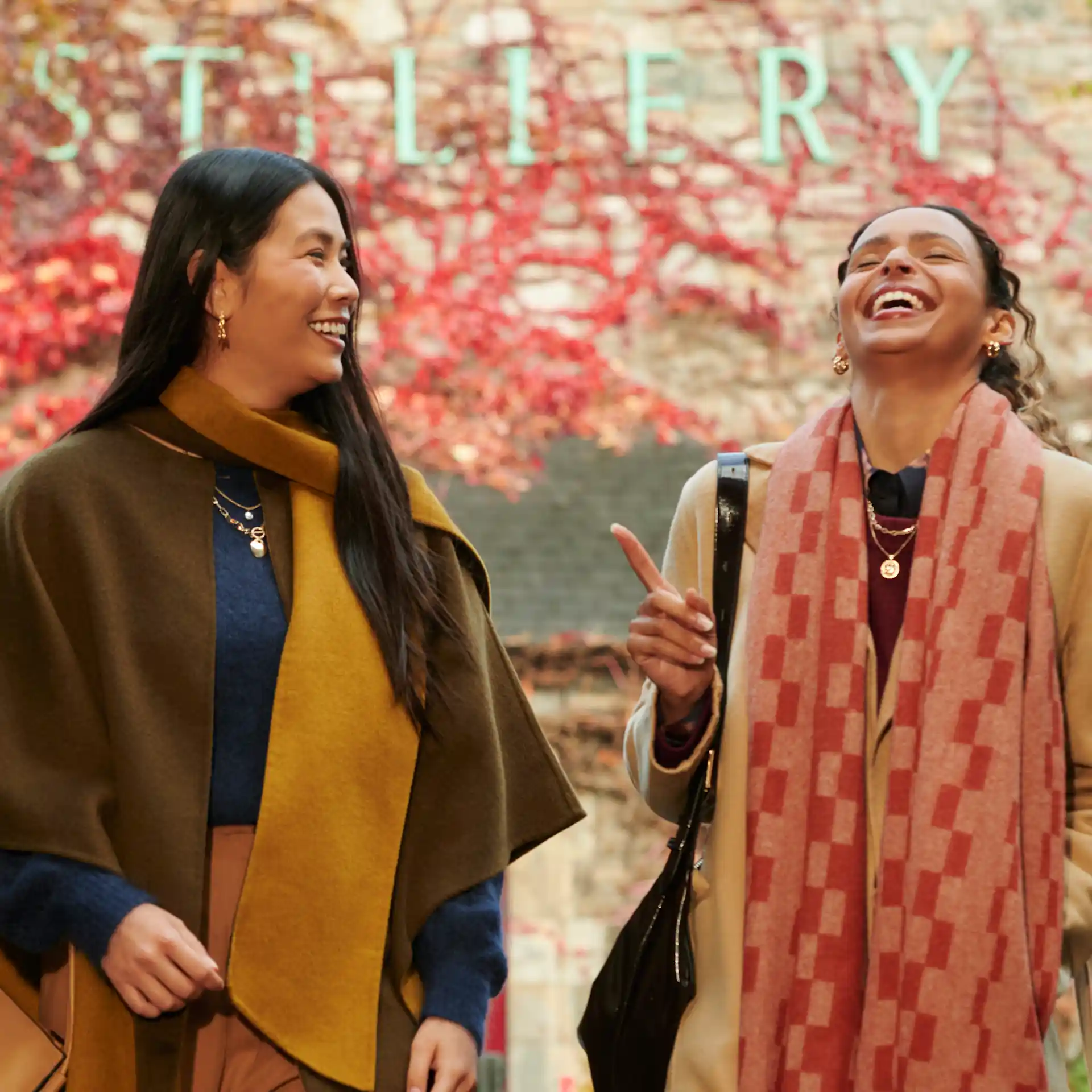 Two female friends stand in front of Blair Athol distillery, laughing together