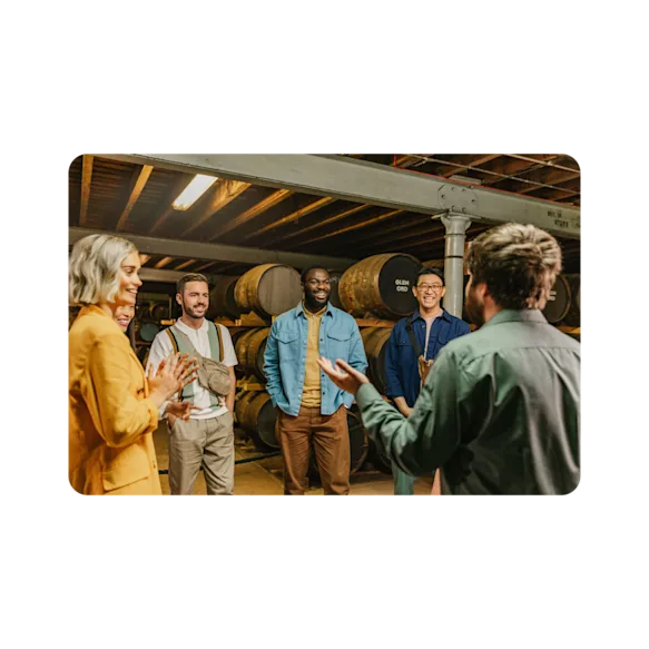 A smiling group surrounded by casks of The Singleton are engaged by a tour guide.