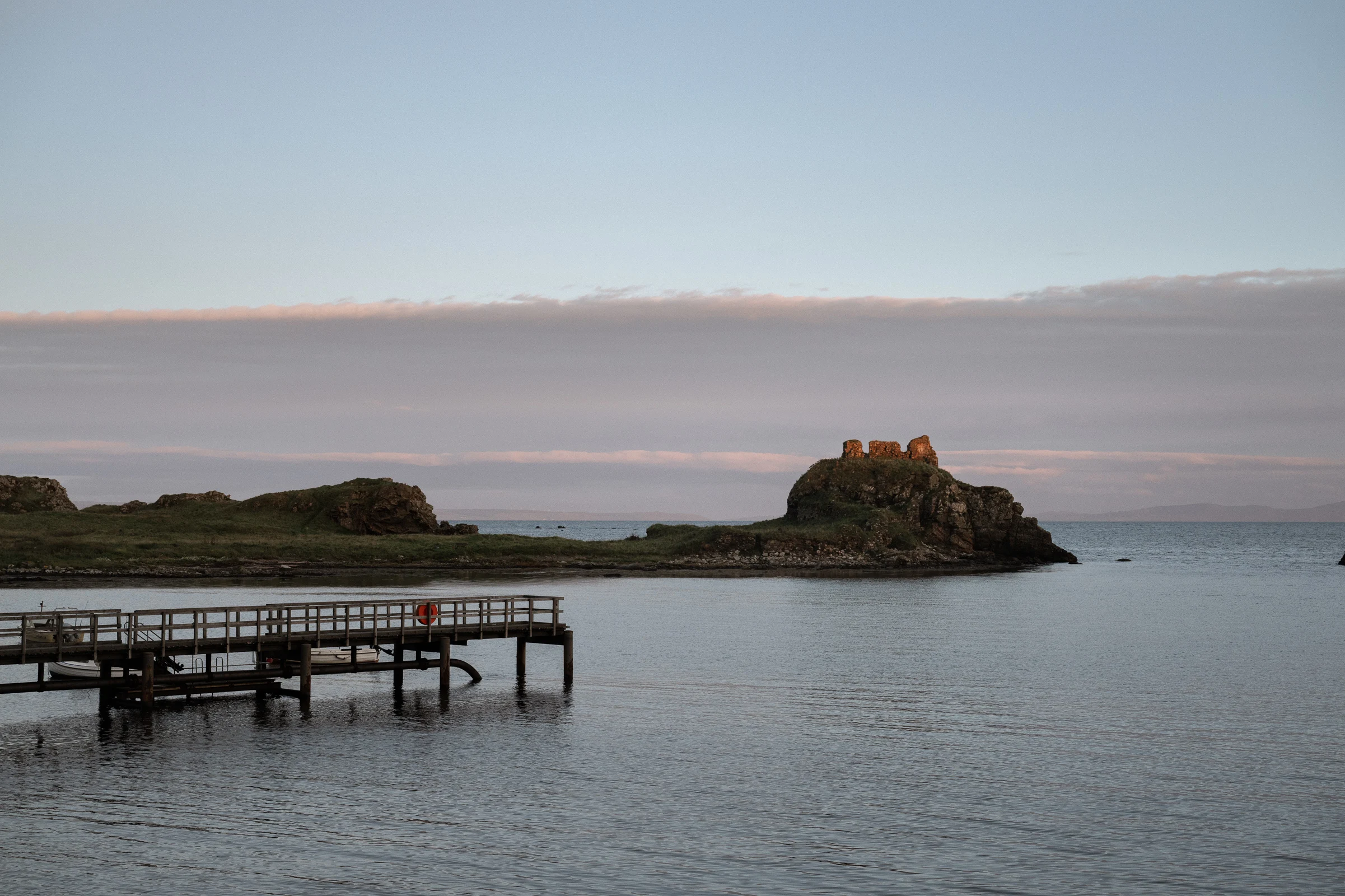 A rocky island outcrop reflected in the calm waters of a sea loch on the Isle of Islay at dusk, with moody skies overhead.