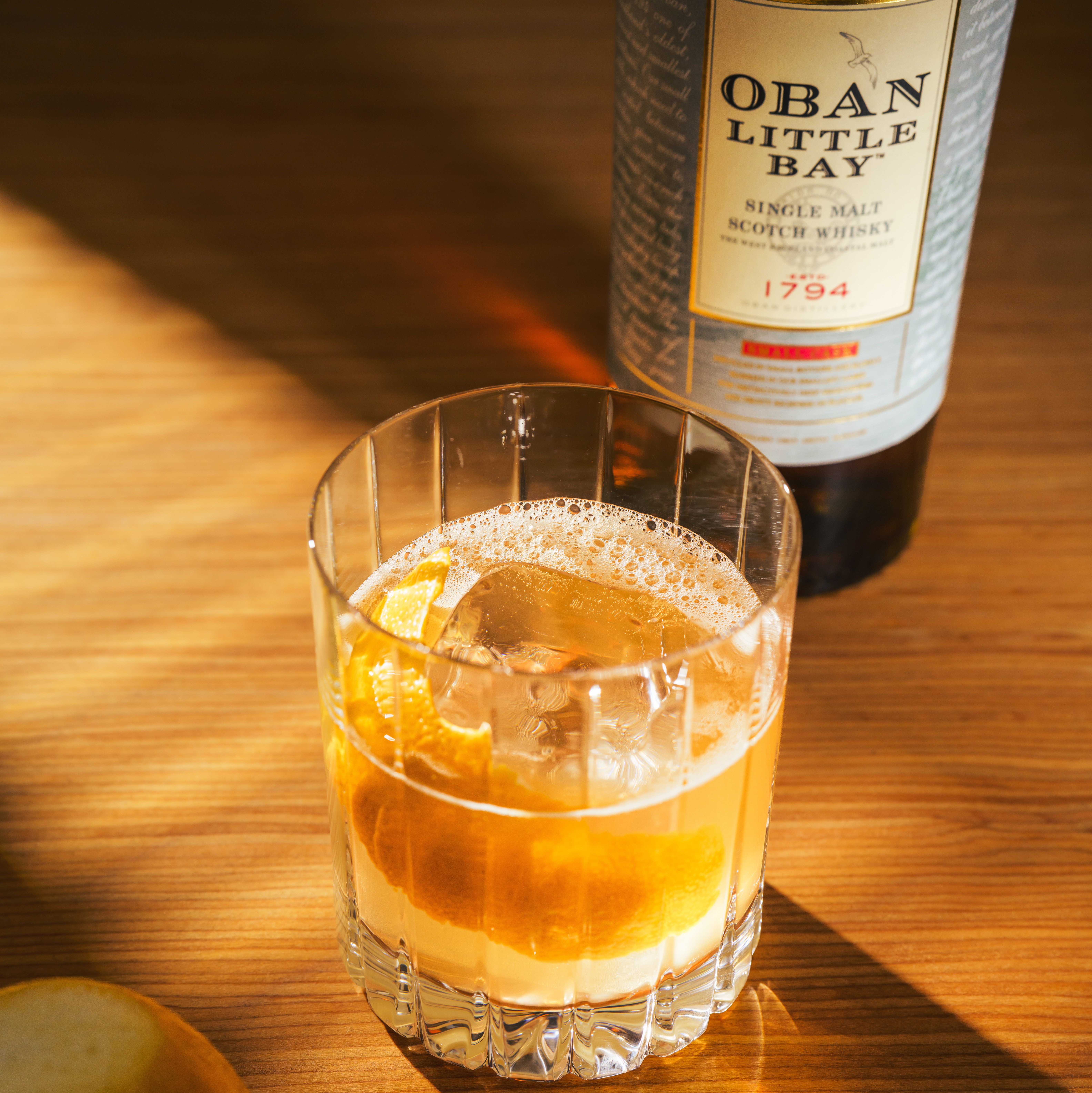 Image of a Highland Gold cocktail with a bottle of Oban Little Bay