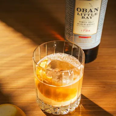 Image of a Highland Gold cocktail with a bottle of Oban Little Bay