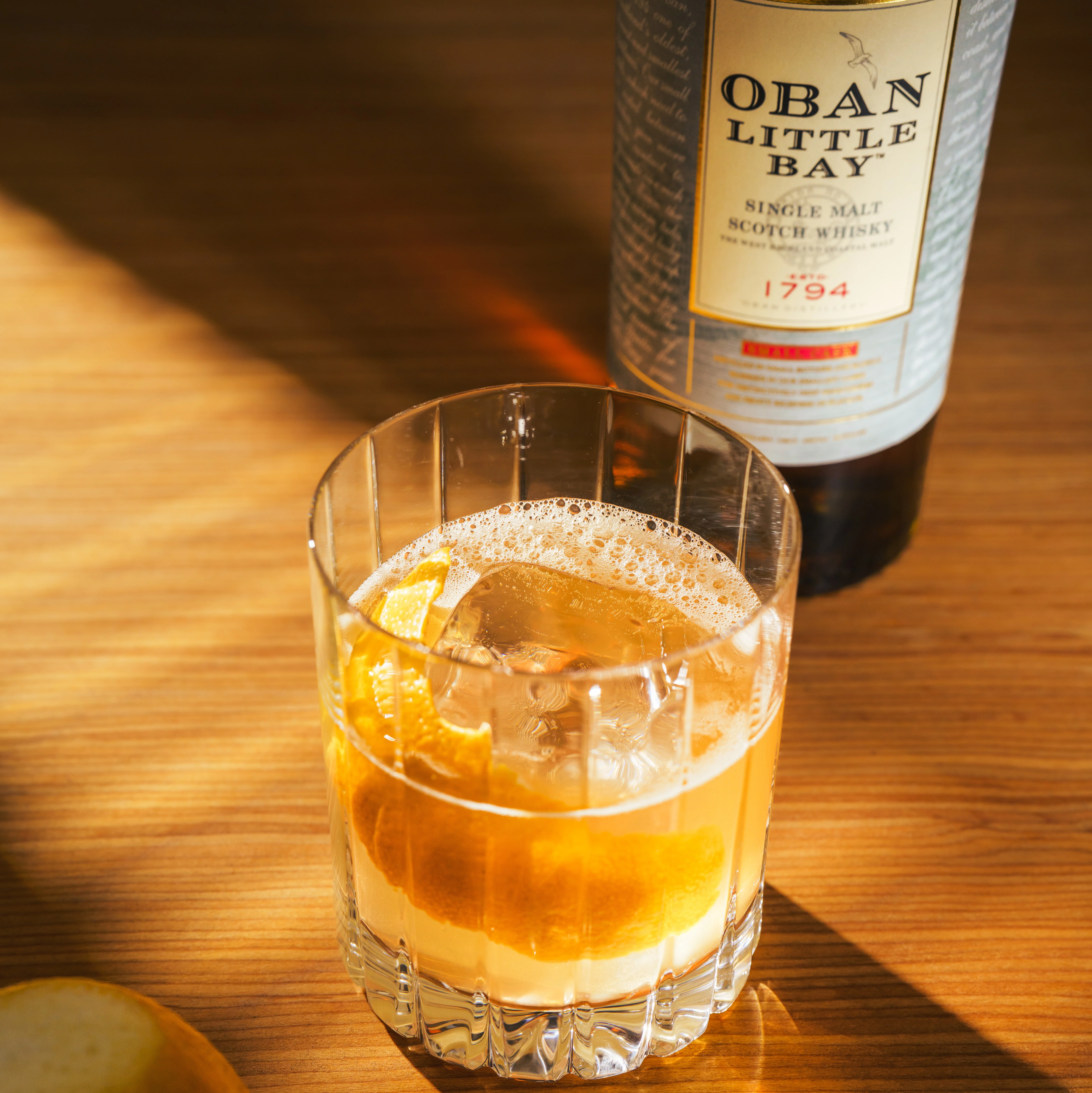 Image of a Highland Gold cocktail with a bottle of Oban Little Bay