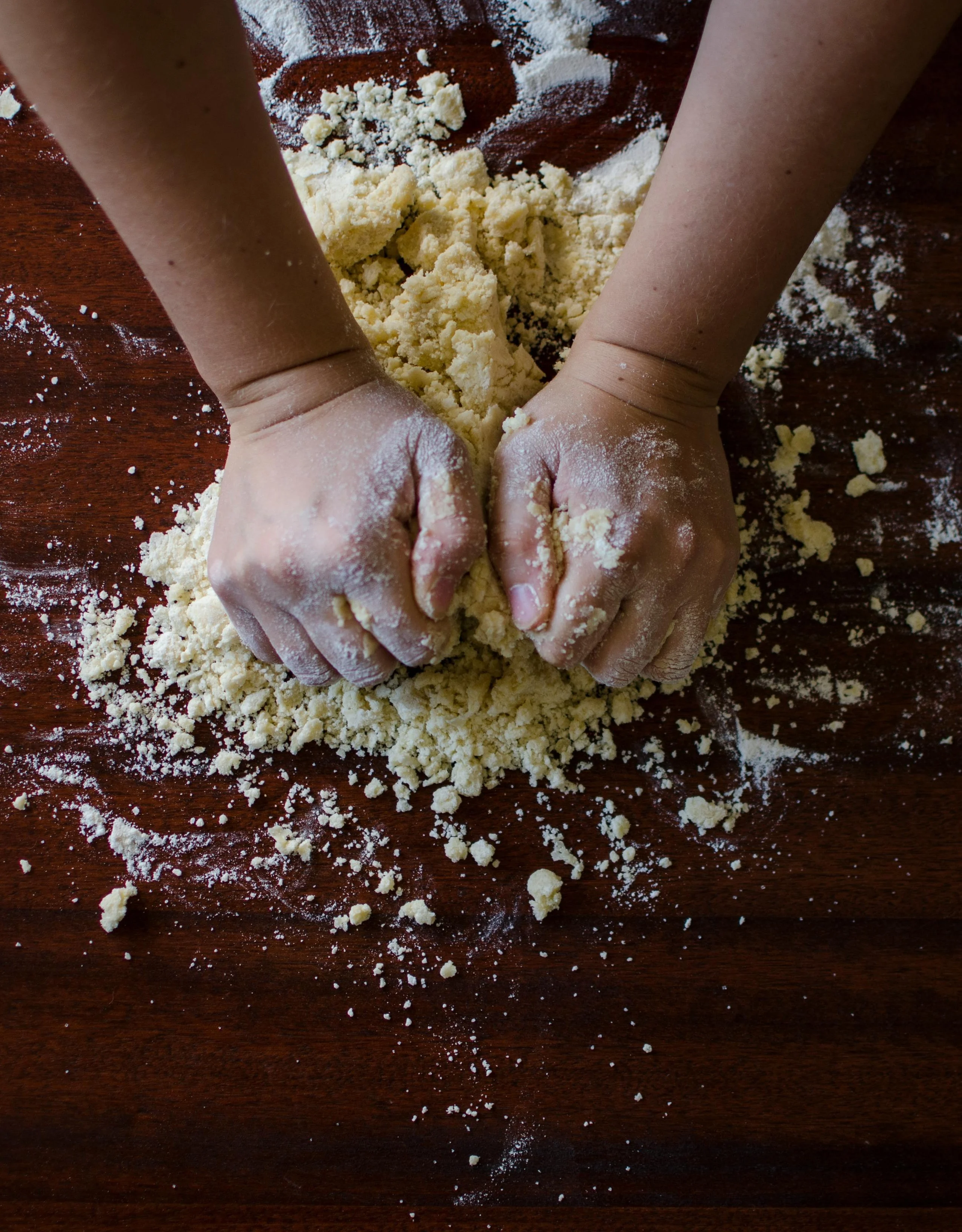 Hands kneading dough on a bench covered in flour.