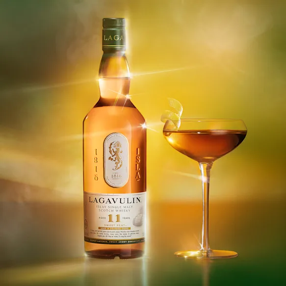 Bottle and glass of Lagavulin 11 Year Old Sweet Peat Islay Single Malt Scotch Whisky, 750ml on green sunrise background