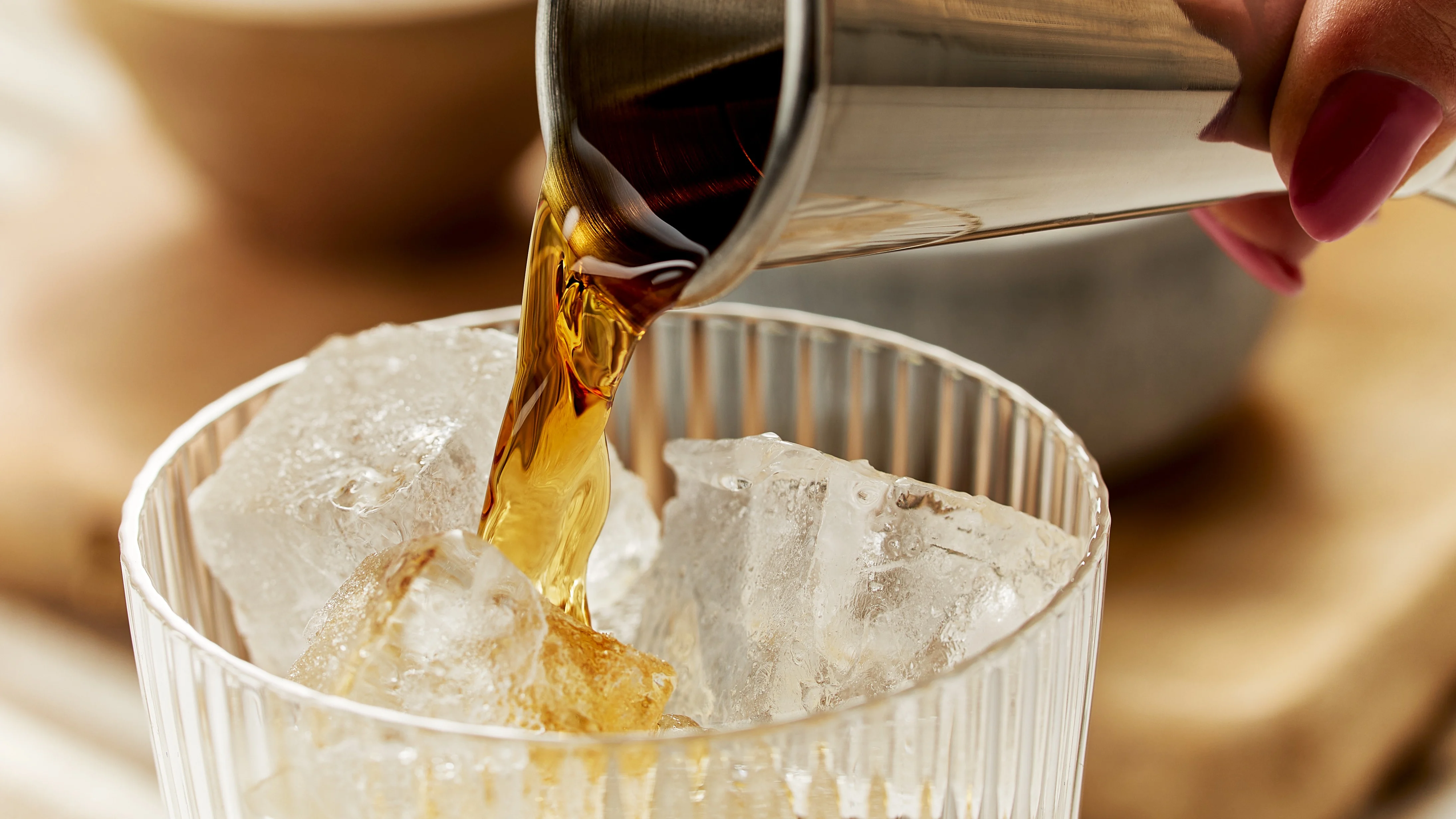 Whisky wird mit einem Jigger in ein mit Eis gefülltes Glas gegossen