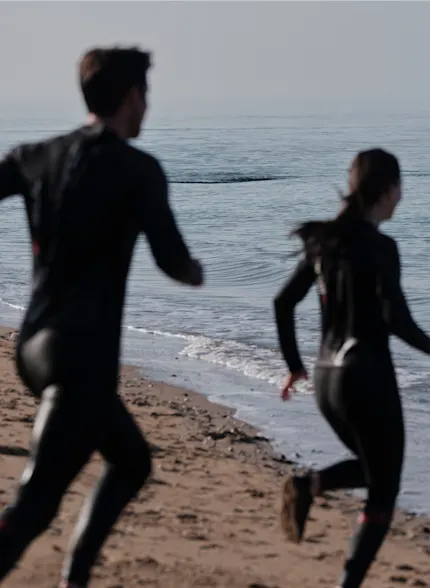 Twee zwemmers in wetsuits rennen naar de oceaan, meedoen aan de Wild Blue Challenge op Wereld Oceaan Dag