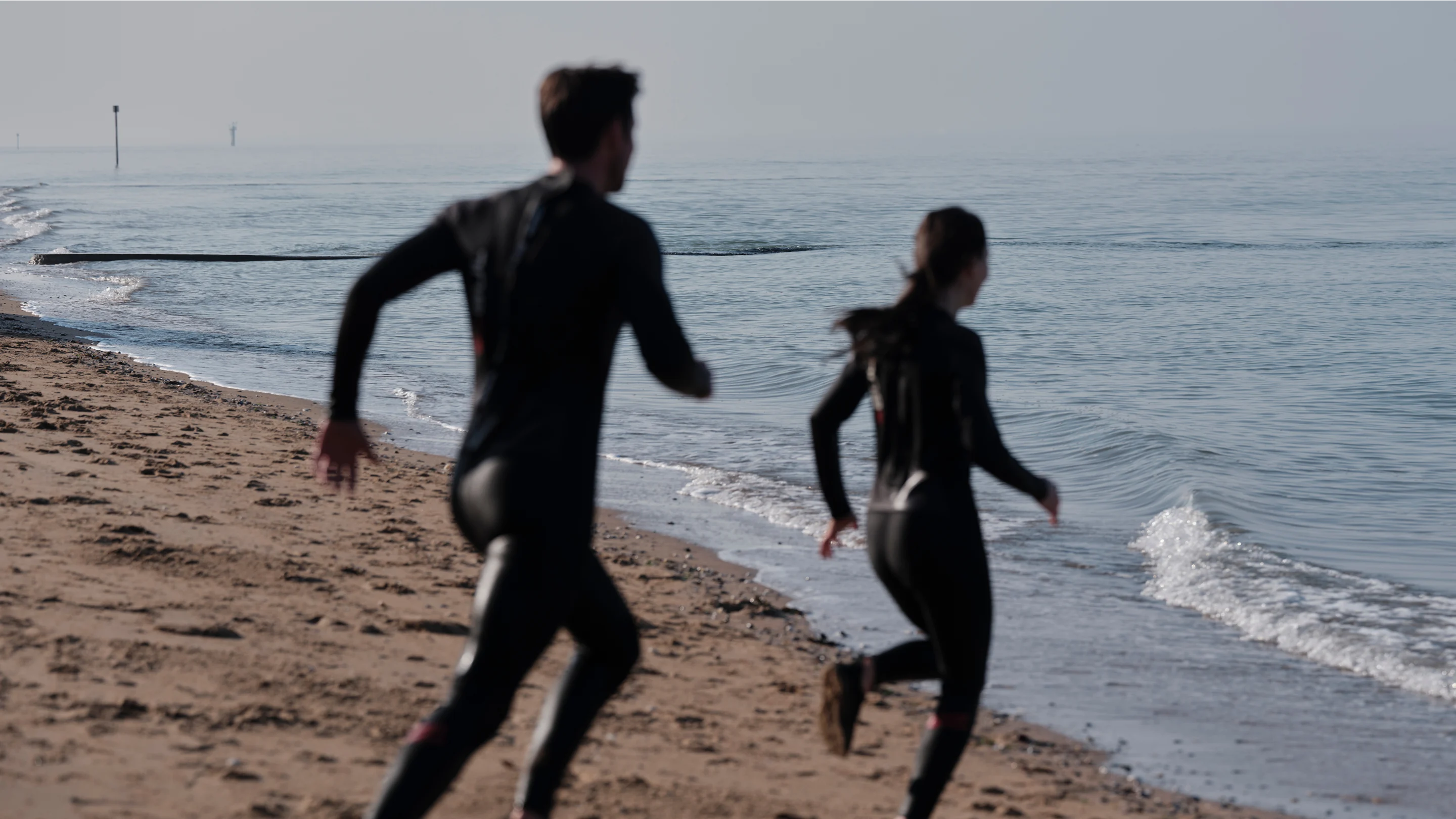 Two swimmers in wetsuits running toward the ocean, participating in The Wild Blue Challenge on World Ocean Day
