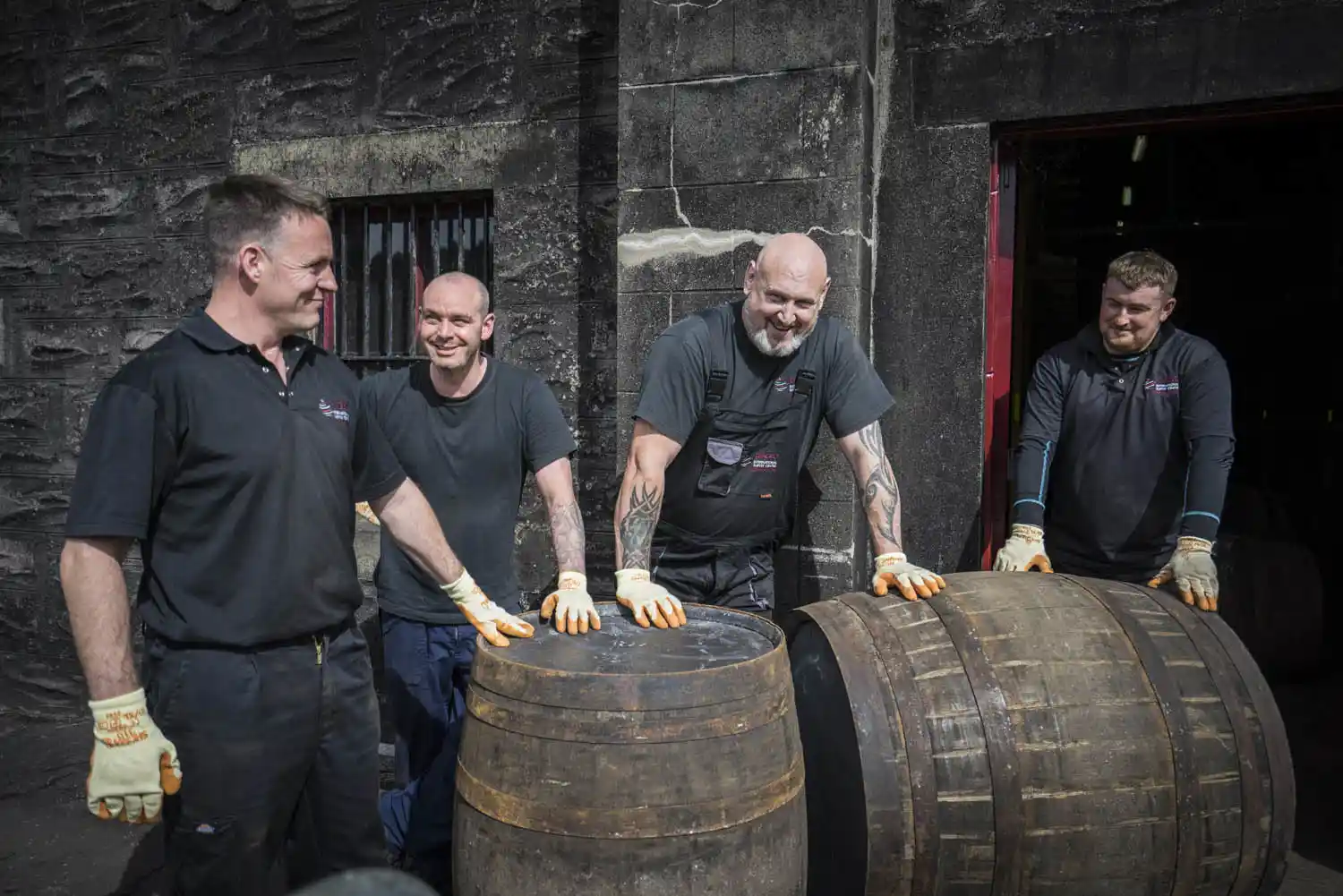 A group of employees stand outside, leaning on two wooden barrels