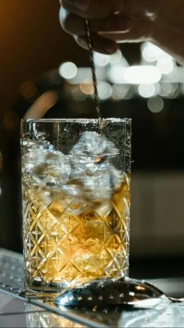 A bartender mixes a Diamondhead cocktail in a tall glass with a long spoon.