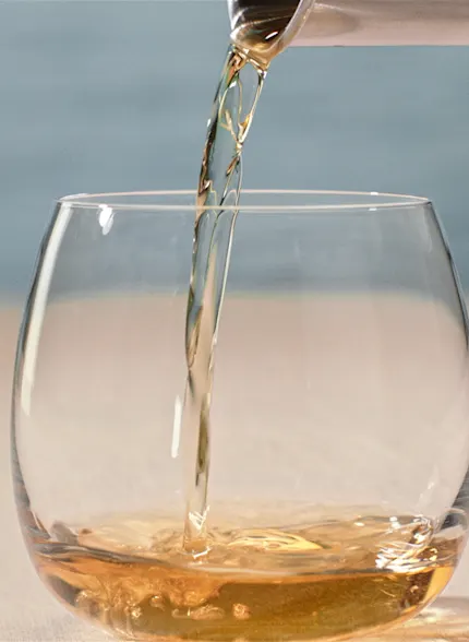 Oban whisky being poured into a round glass with sea in the background