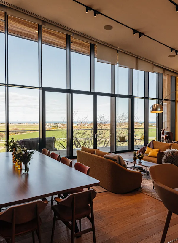 The inside of Clynelish’s visitor centre which features wooden panelling, armchairs, sofas, a bar and a coffee table. One wall has floor to ceiling windows which open onto a balcony which overlooks green fields.