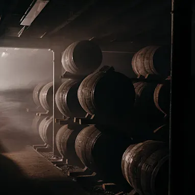 A whisky barrel store stands in the dark, with a shaft of light illuminating a few of the barrels.