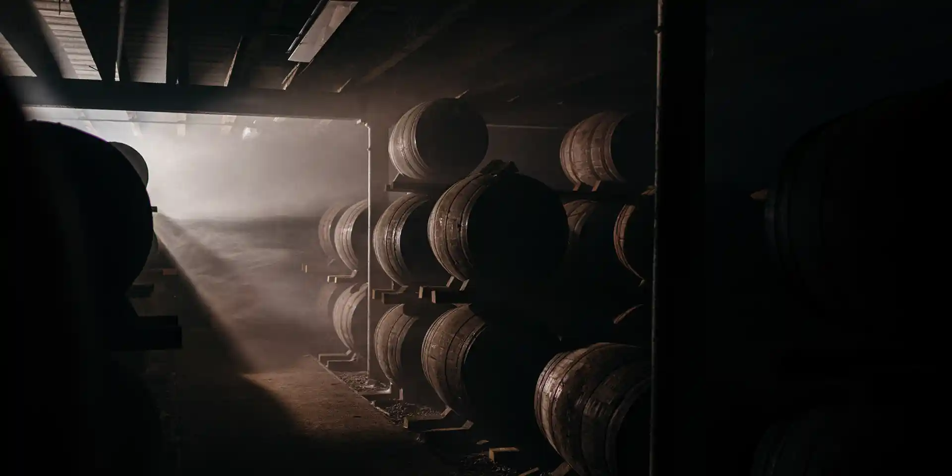 A whisky barrel store stands in the dark, with a shaft of light illuminating a few of the barrels.