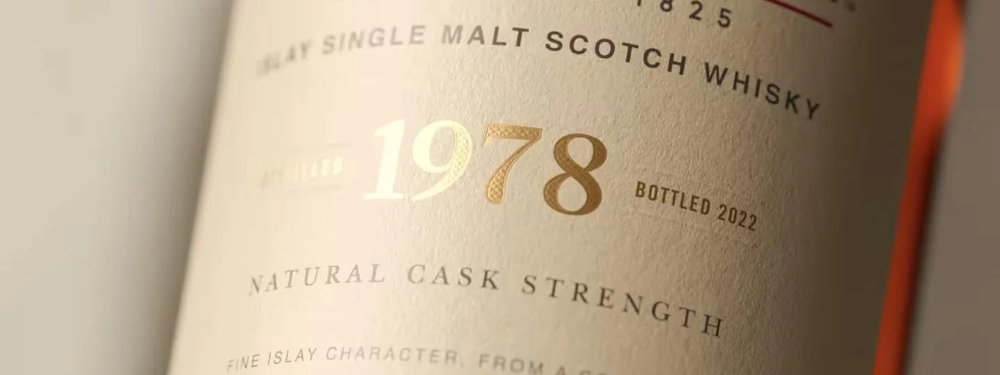 A bottle of Port Ellen whisky lies label-up on a neutral backdrop.