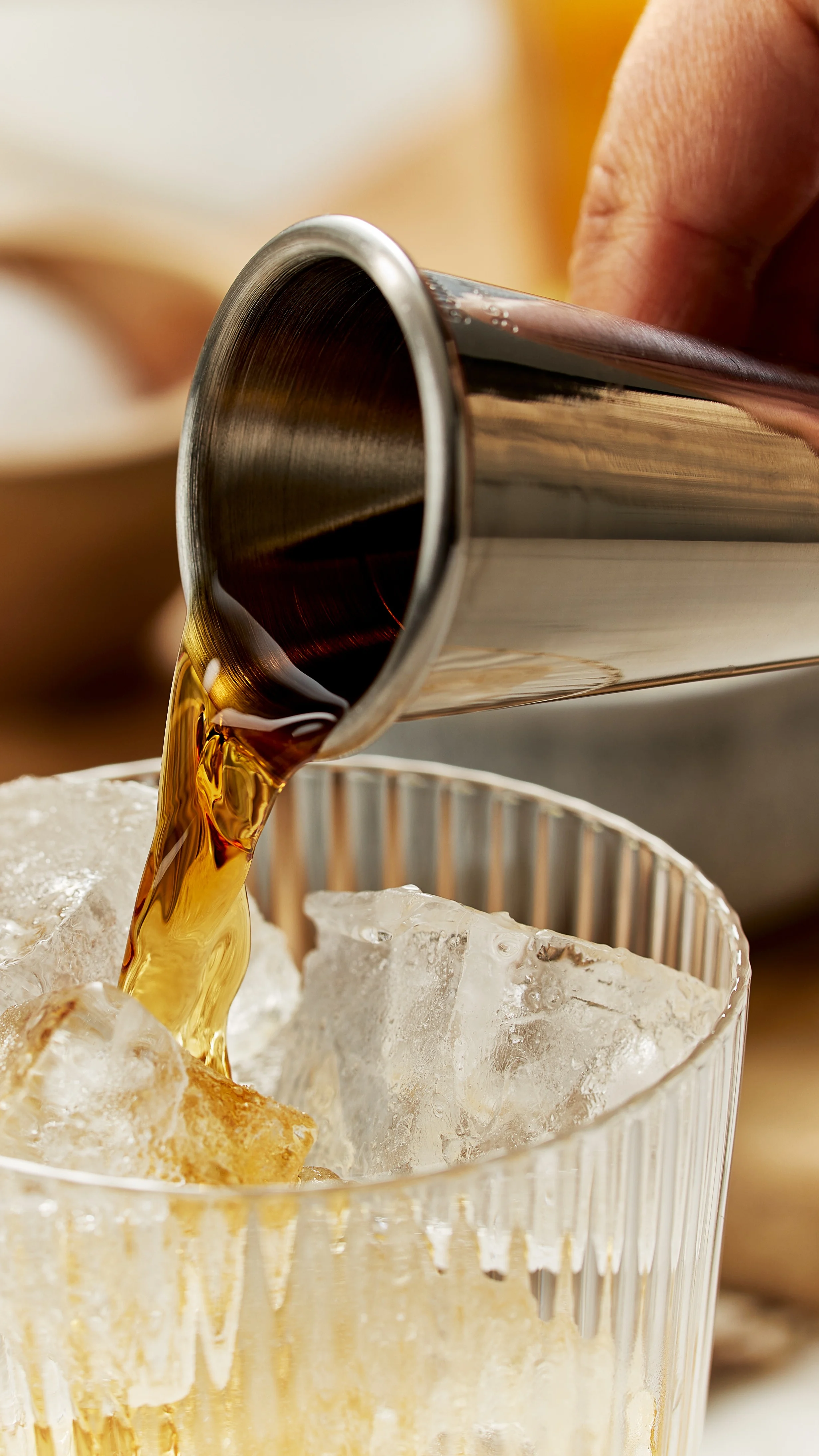 Whisky wird mit einem Jigger in ein mit Eis gefülltes Glas gegossen