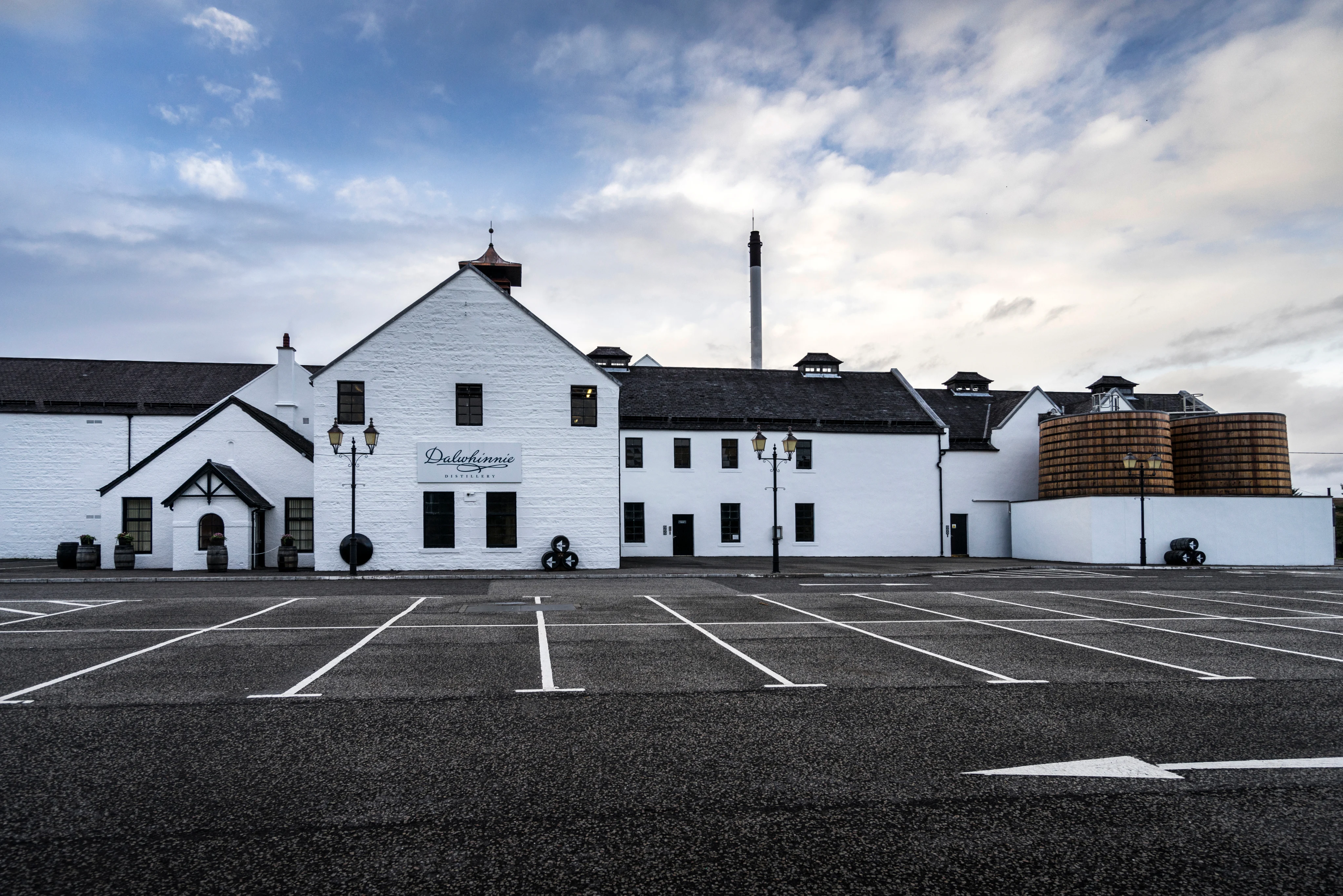 Exterior of Dalwhinnie Distillery with its iconic white-washed stone buildings, traditional pagoda chimney and wooden washbacks visible under a dramatic Scottish sky