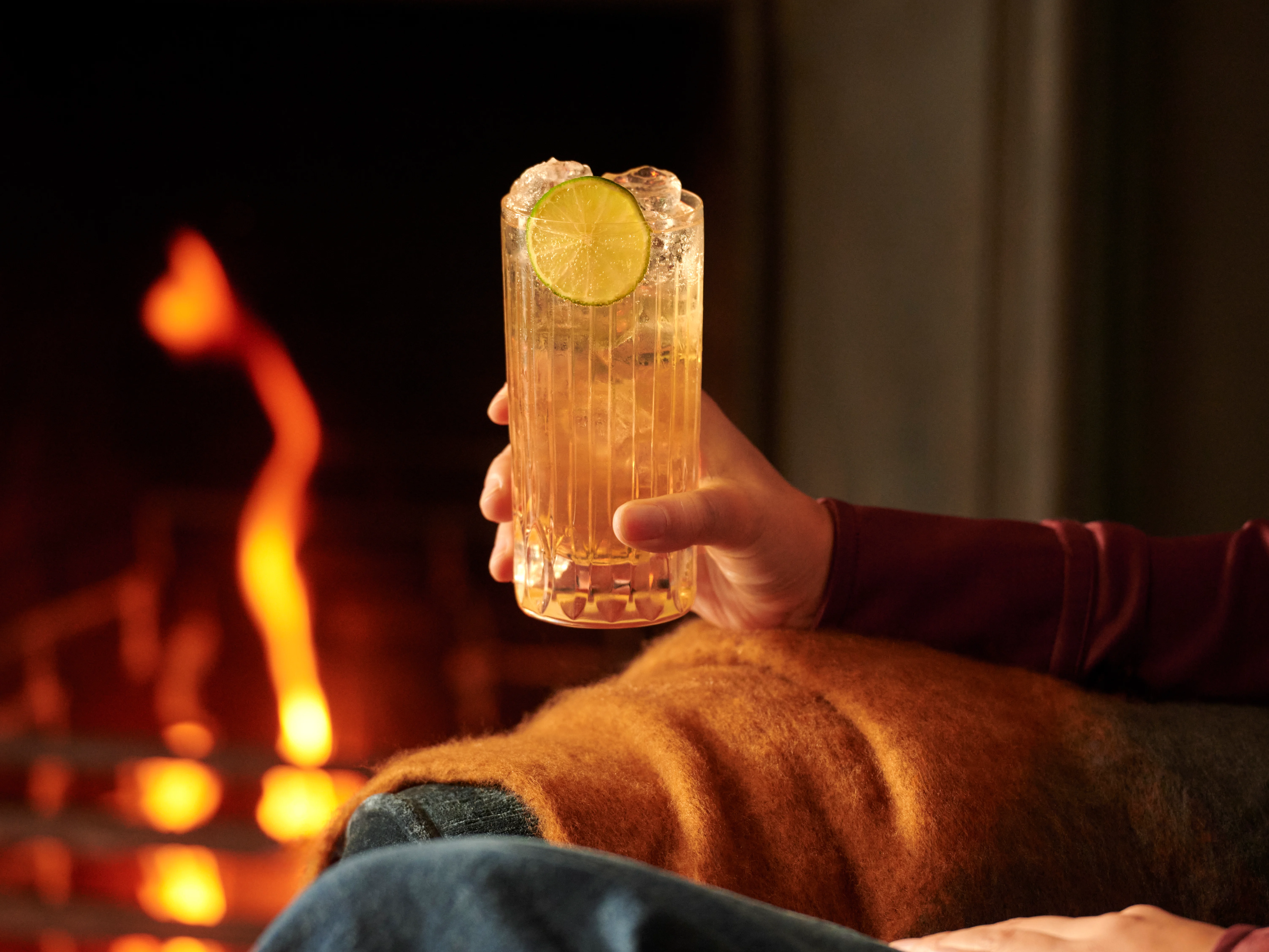 A woman holds a whisky highball next to a fire
