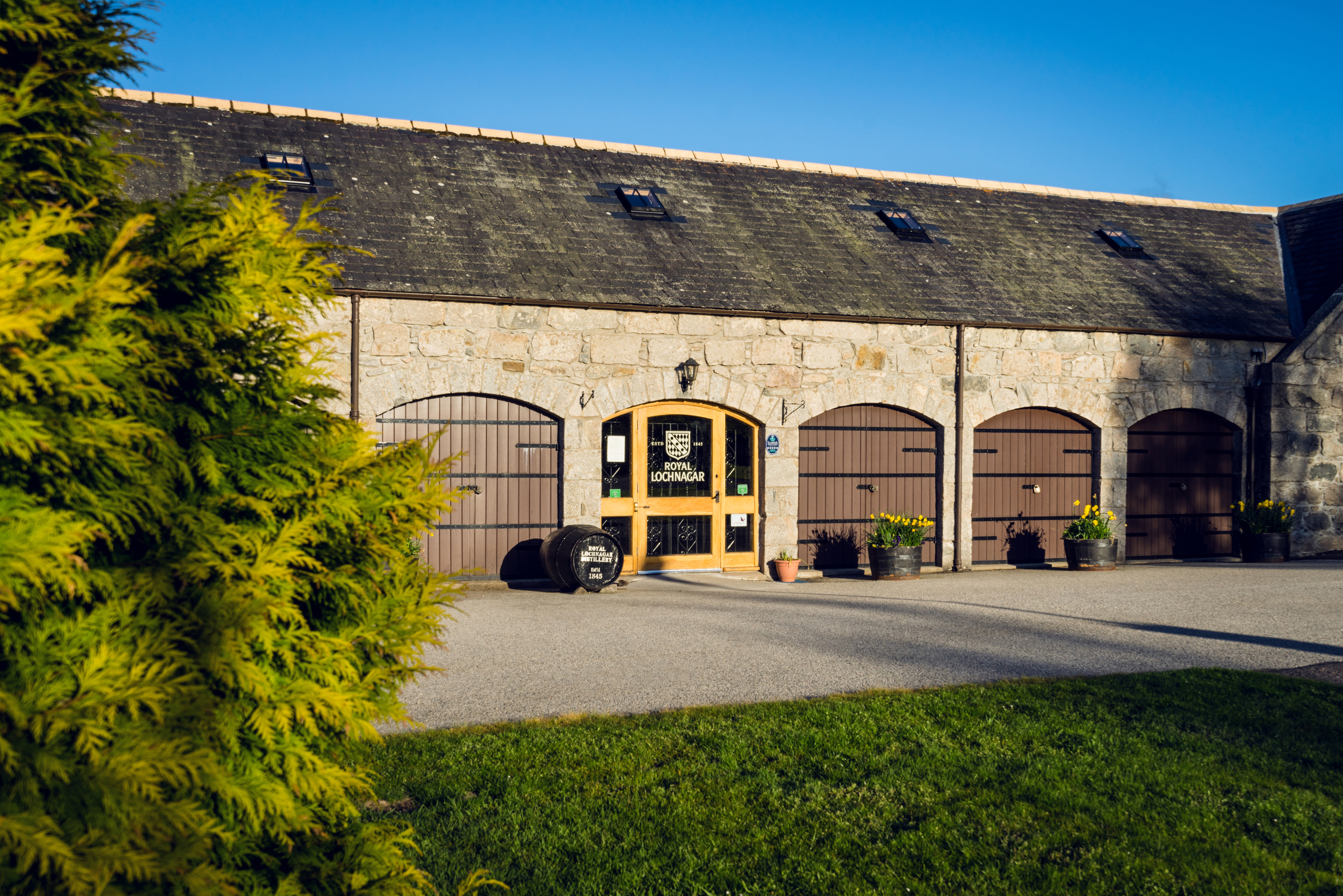 Front view of the Royal Lochnagar distillery showing visitor entrance, front garden and a nice blue sky