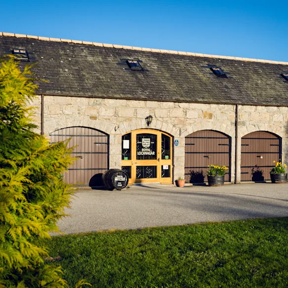 Front view of the Royal Lochnagar distillery showing visitor entrance, front garden and a nice blue sky