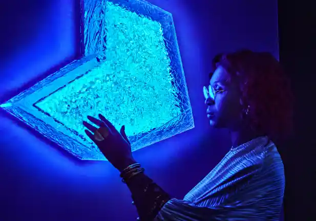 A woman stands next to a neon blue sign attached to a wall, placing a hand on the sign.