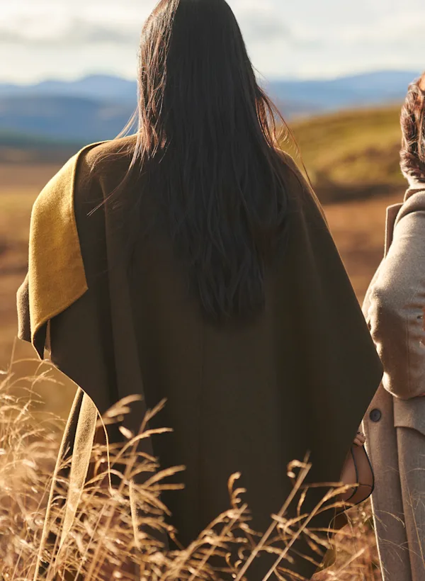 Two friends look out over the Highlands in autumn. In the background are several hills covered in golden grass.