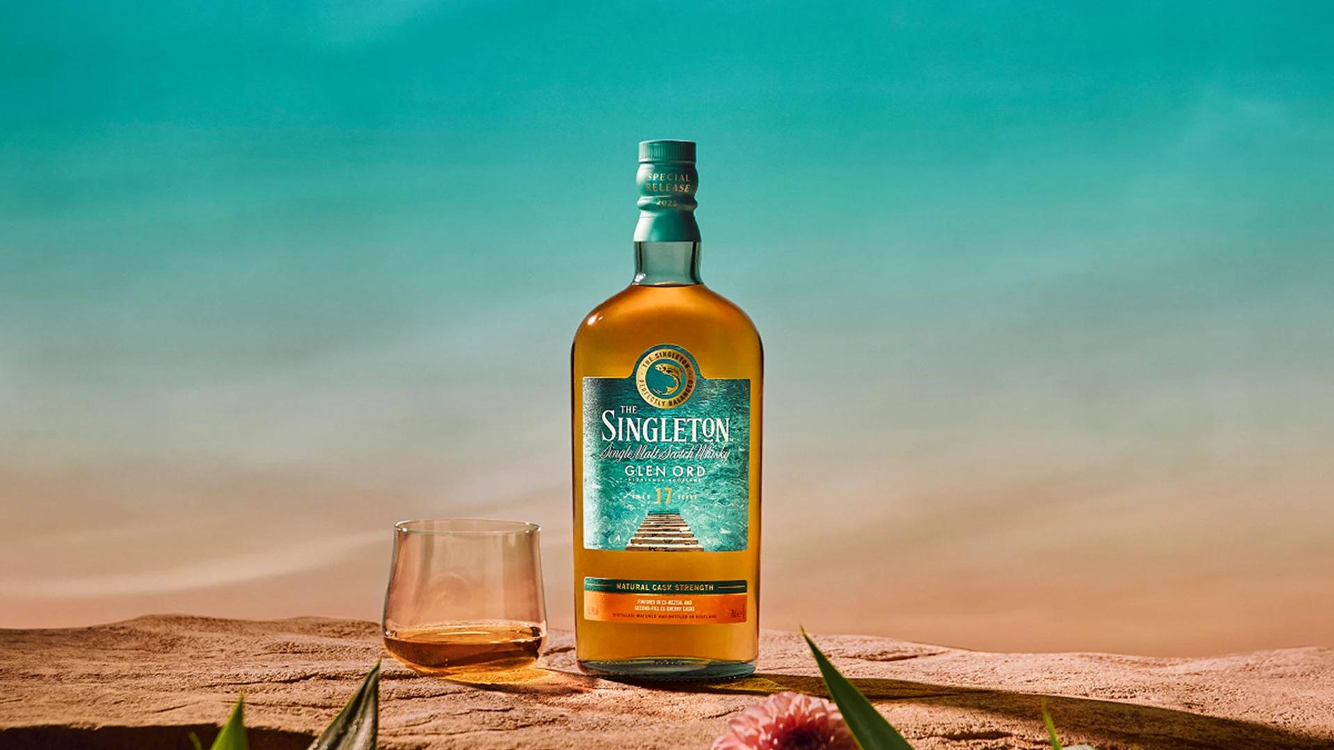 The Singleton Glen Ord whisky bottle with dram glass on sand and tropical flowers