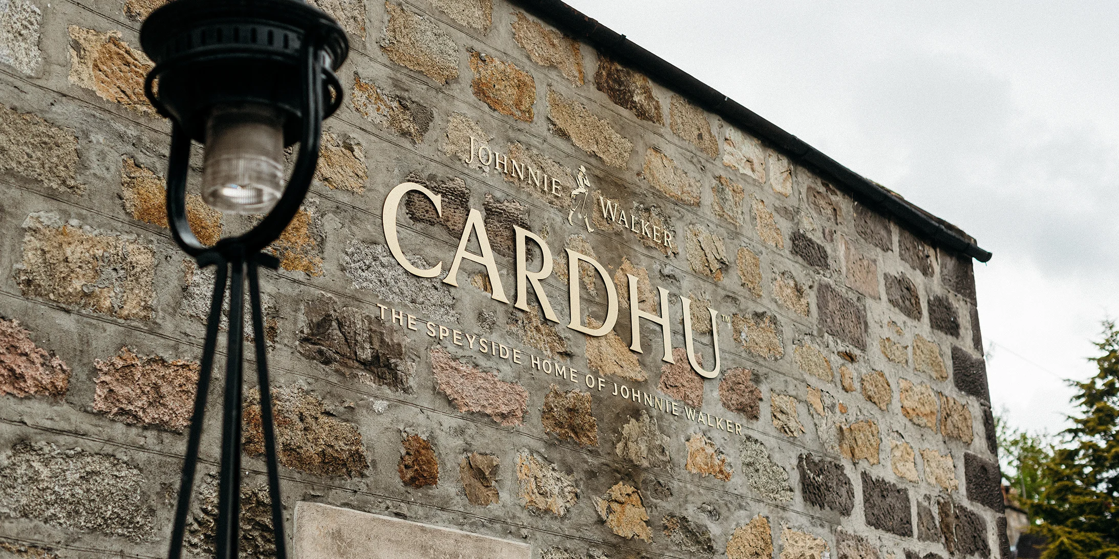 A brick wall shows a golden sign saying Cardhu, with a black lantern standing by the wall.