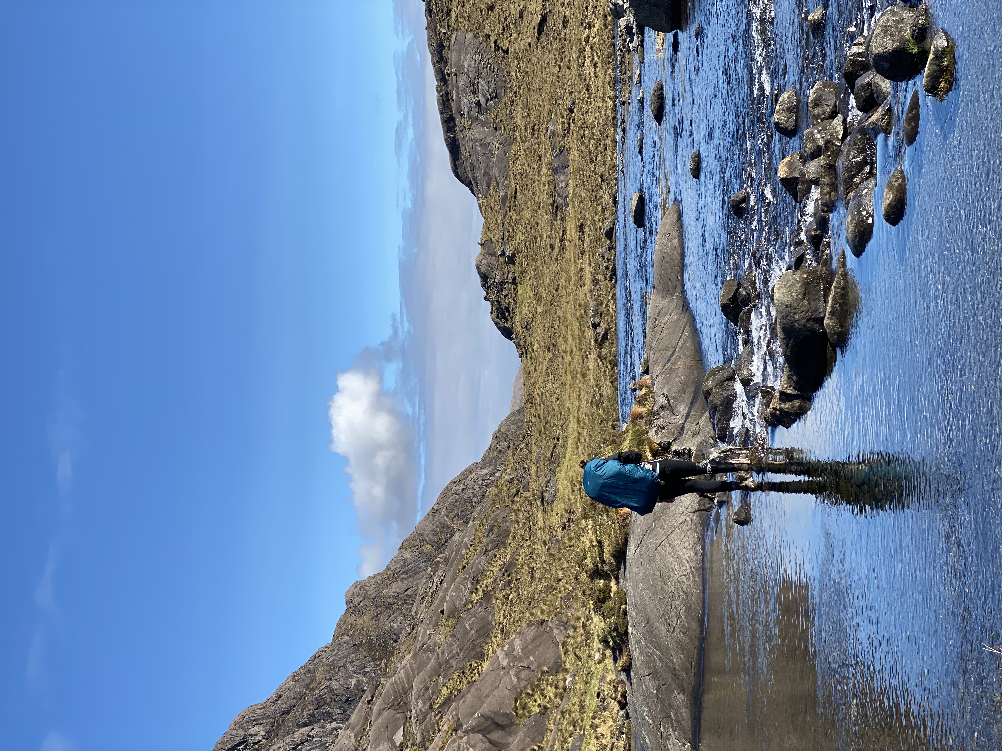 A person walks through a stream against the backdrop of a mountain range.