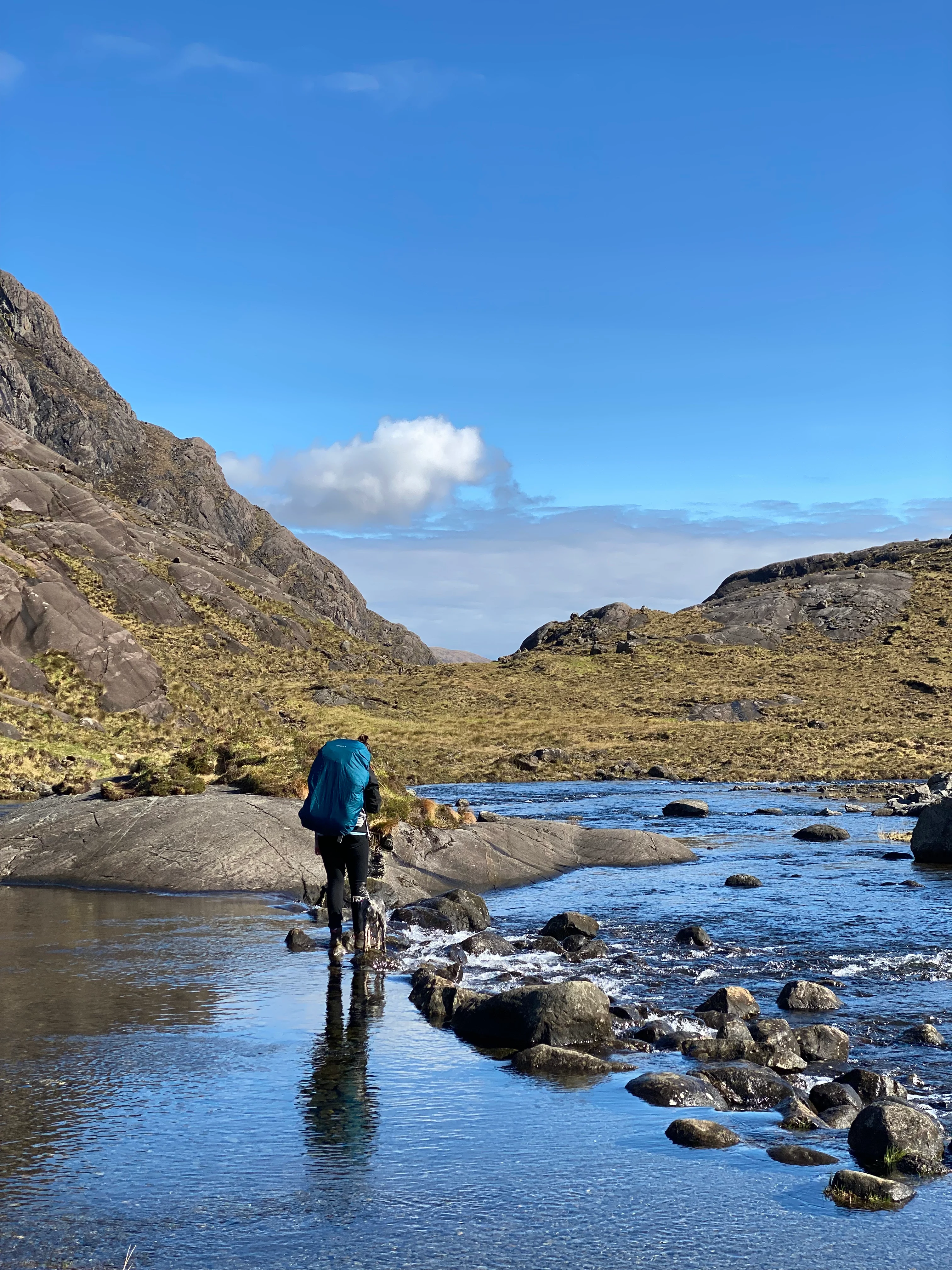 A person walks through a stream against the backdrop of a mountain range. 