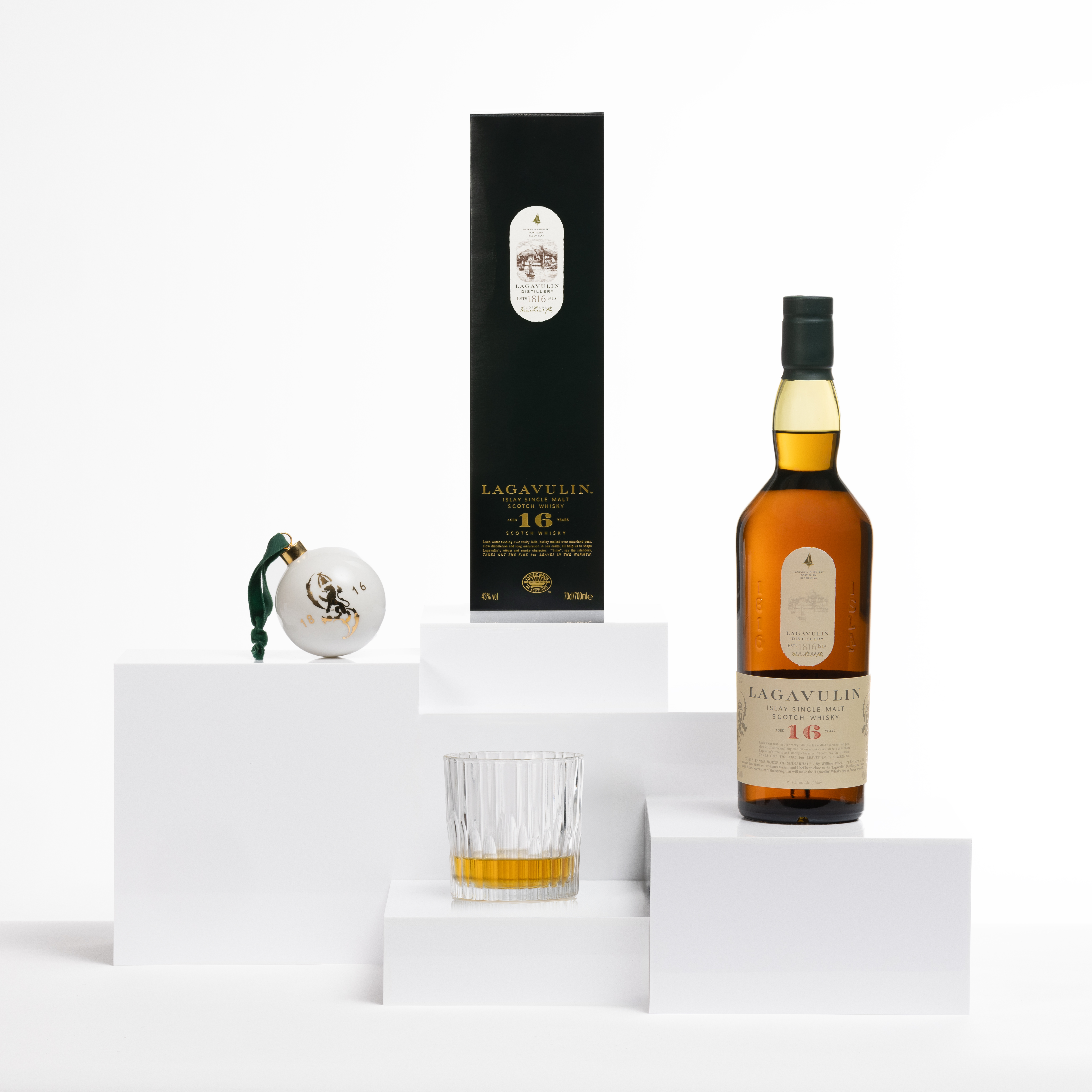 Een Lagavulin 16 fles met verpakking en een witte merkbal met gouden accenten.