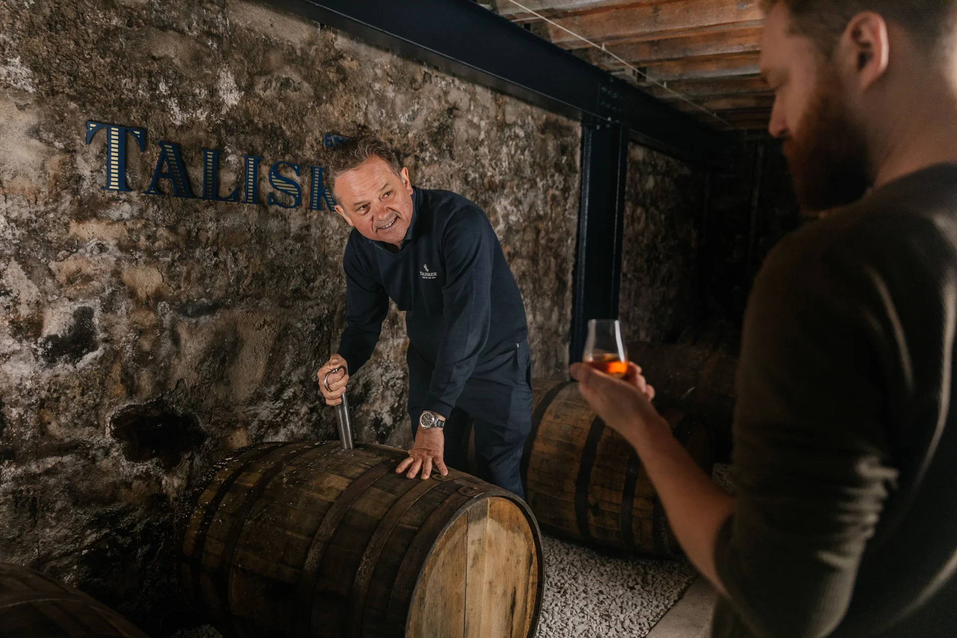 Ein Talisker-Mitarbeiter zeigt einem Gast bei einer Brennereibesichtigung ein Whisky-Fass