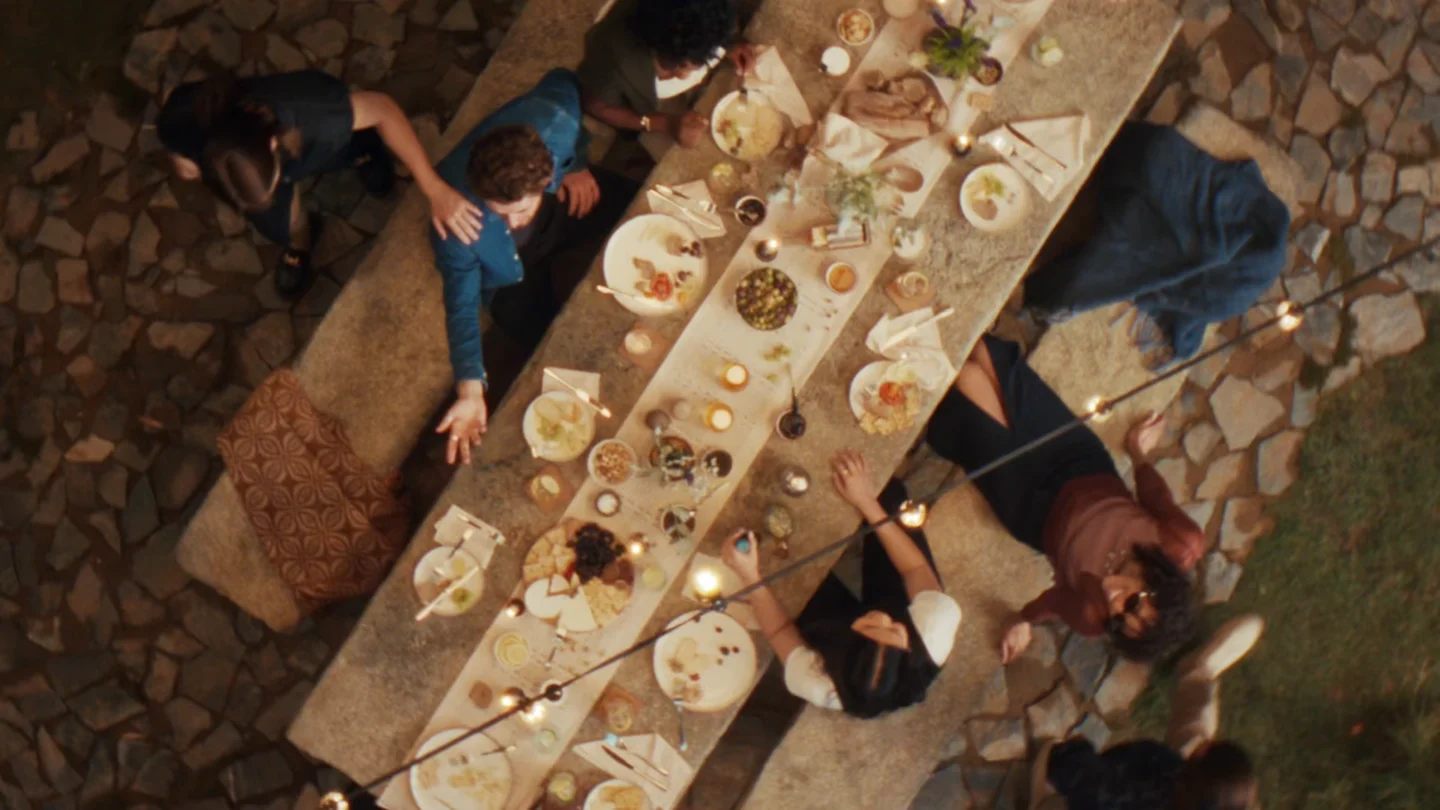 Blick von oben auf einen rustikalen Esstisch im Freien mit Menschen, die Essen und Getränke genießen