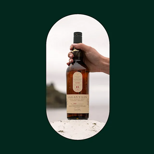 Hand placing a Lagavulin whisky bottle on a white rock on Islay