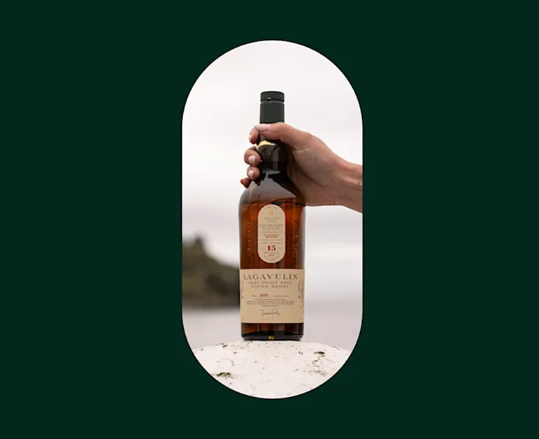 Hand placing a Lagavulin whisky bottle on a white rock on Islay