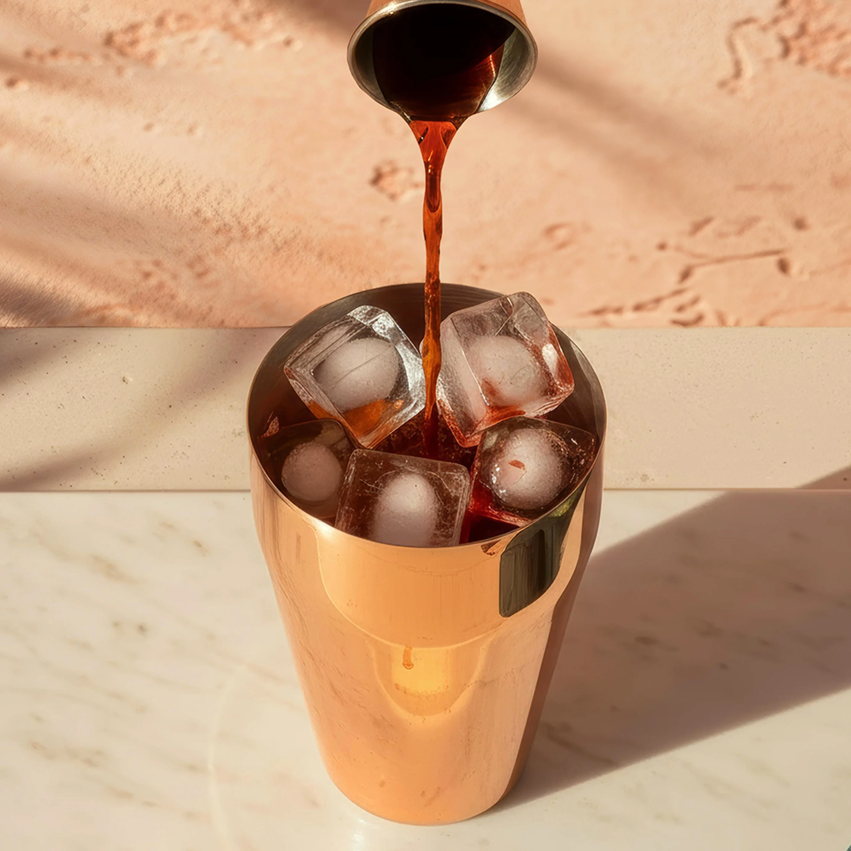 A brown liquid is poured into a copper cocktail shaker over ice, with a bowl of green olives nearby