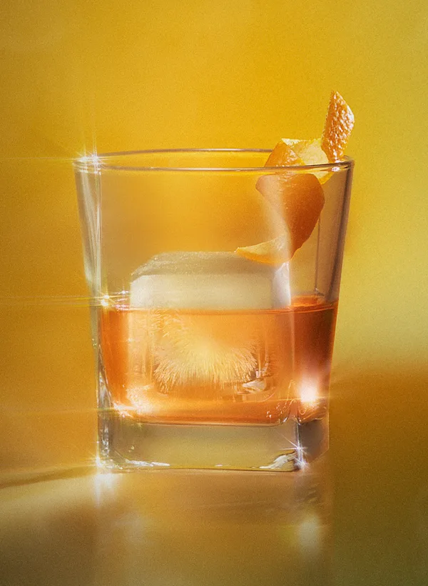 Lagavulin Sweet Peat whisky cocktail served on the rocks with orange peel garnish in a rocks glass on a warm amber background.