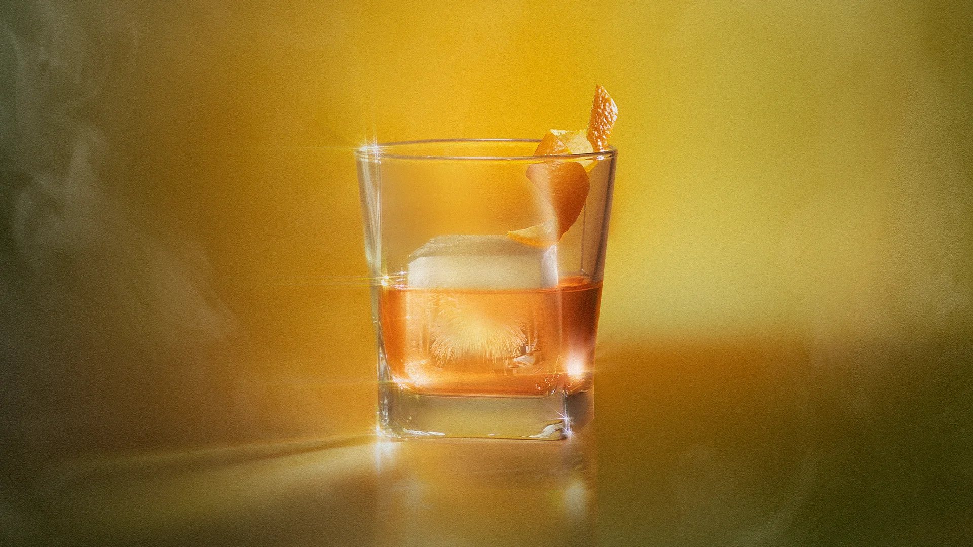 Lagavulin Sweet Peat whisky cocktail served on the rocks with orange peel garnish in a rocks glass on a warm amber background.
