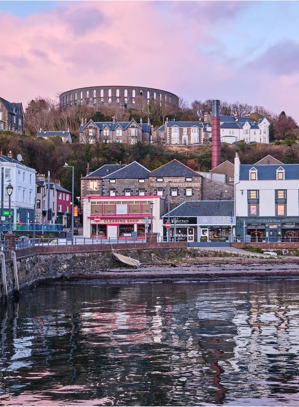 Die Stadt Oban bei Sonnenuntergang mit den rosa Wolken, die sich auf dem Wasser spiegeln.
