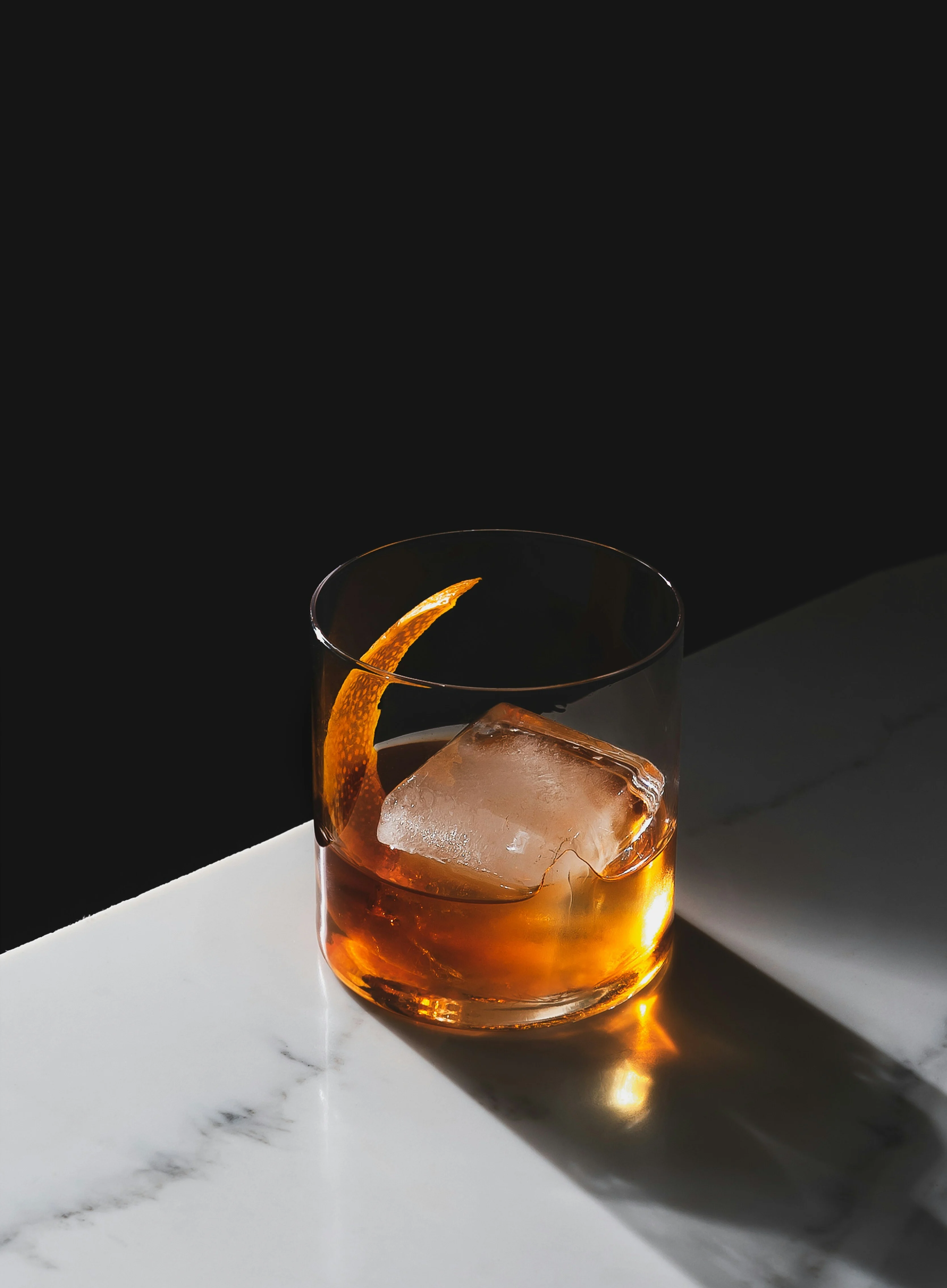 A glass of whisky in a rocks glass with an orange garnish.
