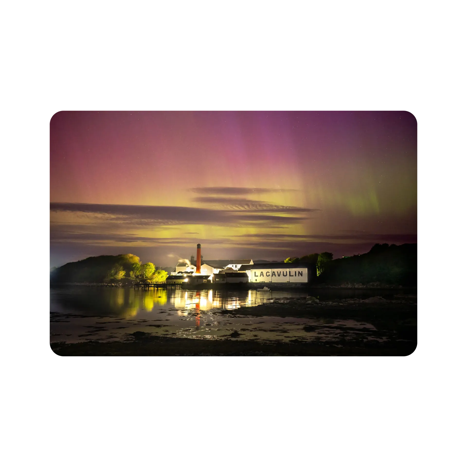 A view at dusk across the bay to Lagavulin's iconic distillery illuminated by bright lights. 