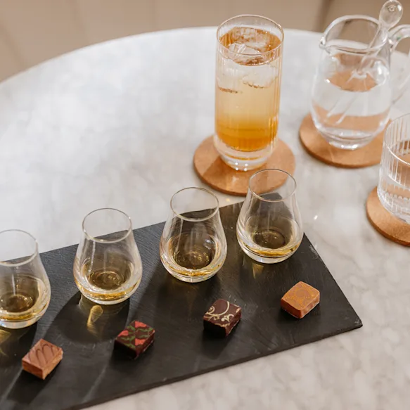 Four whisky dram pairing with four artisanal chocolates. On the side there is a whisky cocktail and a jug and glass of water.