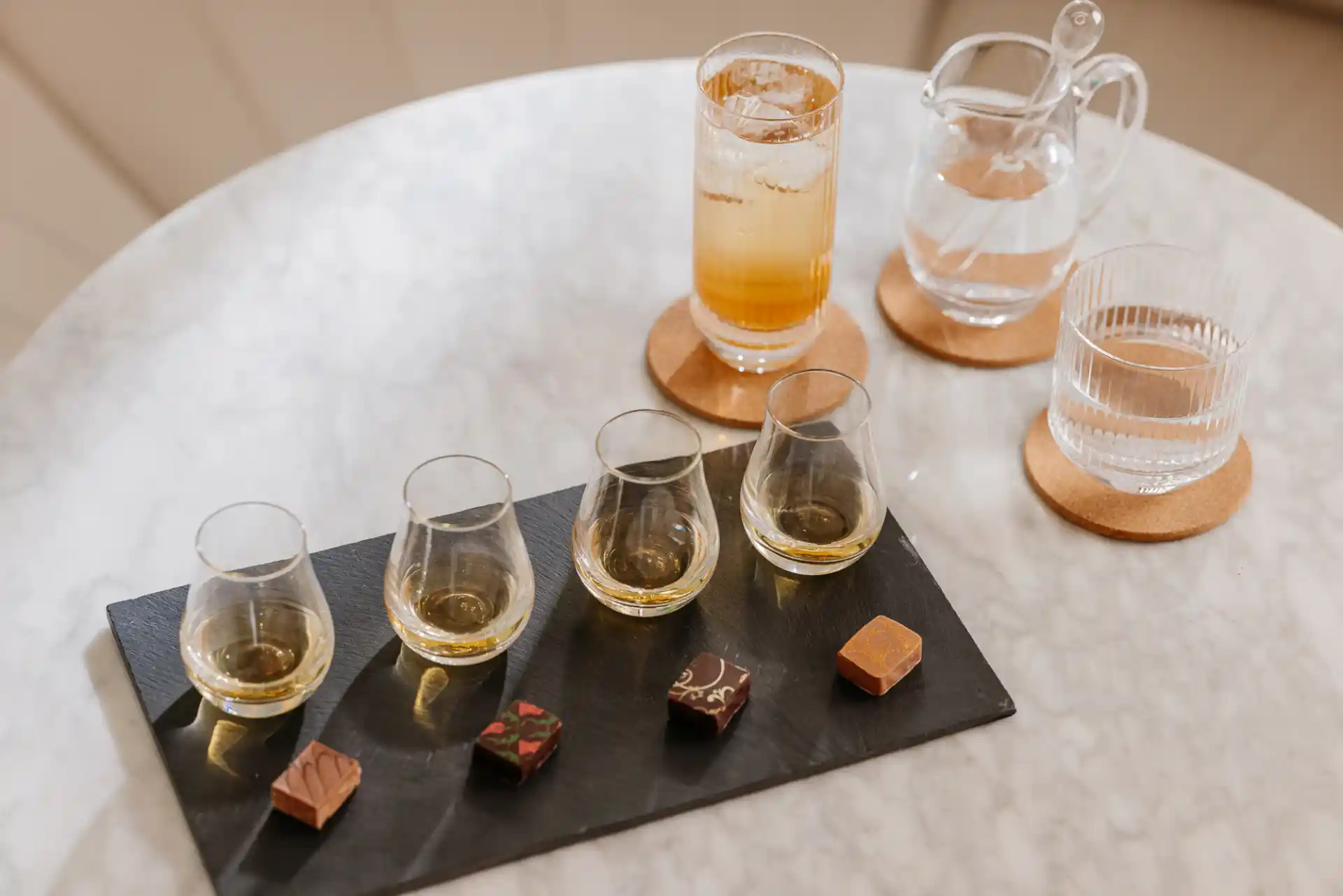 Four whisky dram pairing with four artisanal chocolates. On the side there is a whisky cocktail and a jug and glass of water.